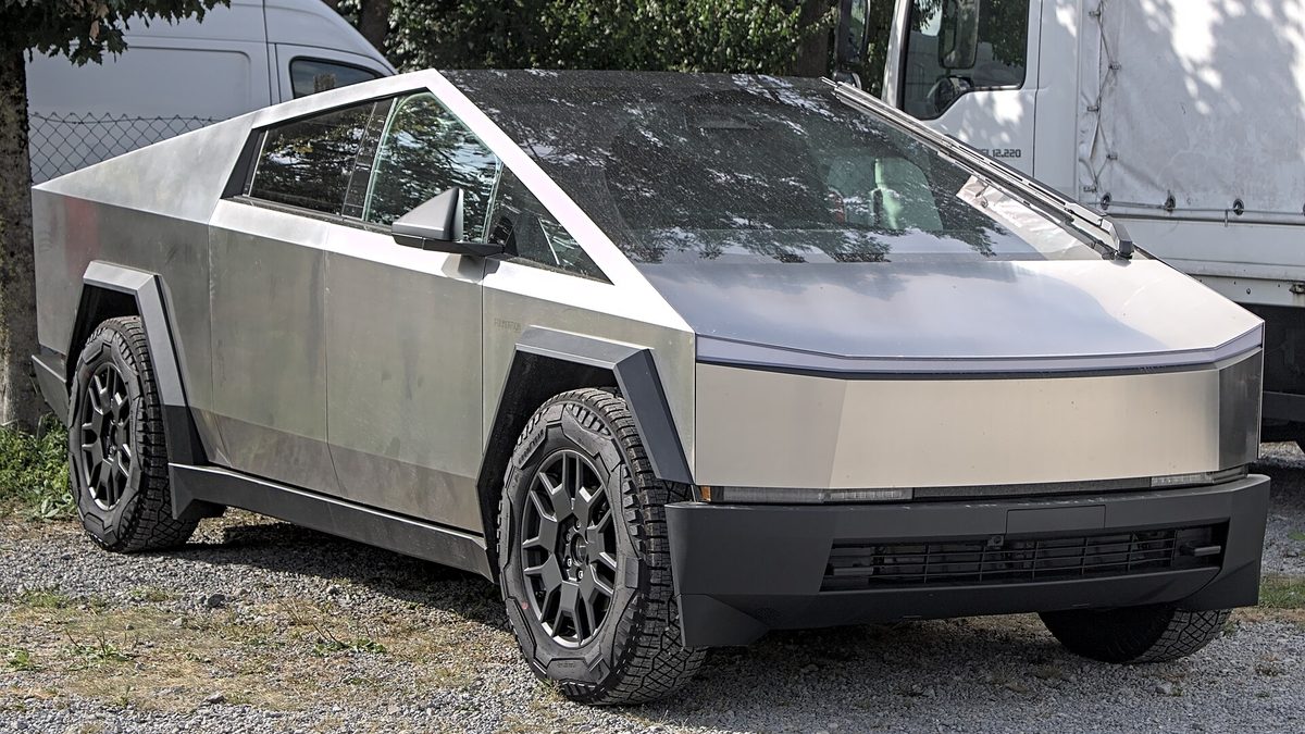 Photo: a stainless steel Tesla Cybertruck parked on gravel, seen from the front